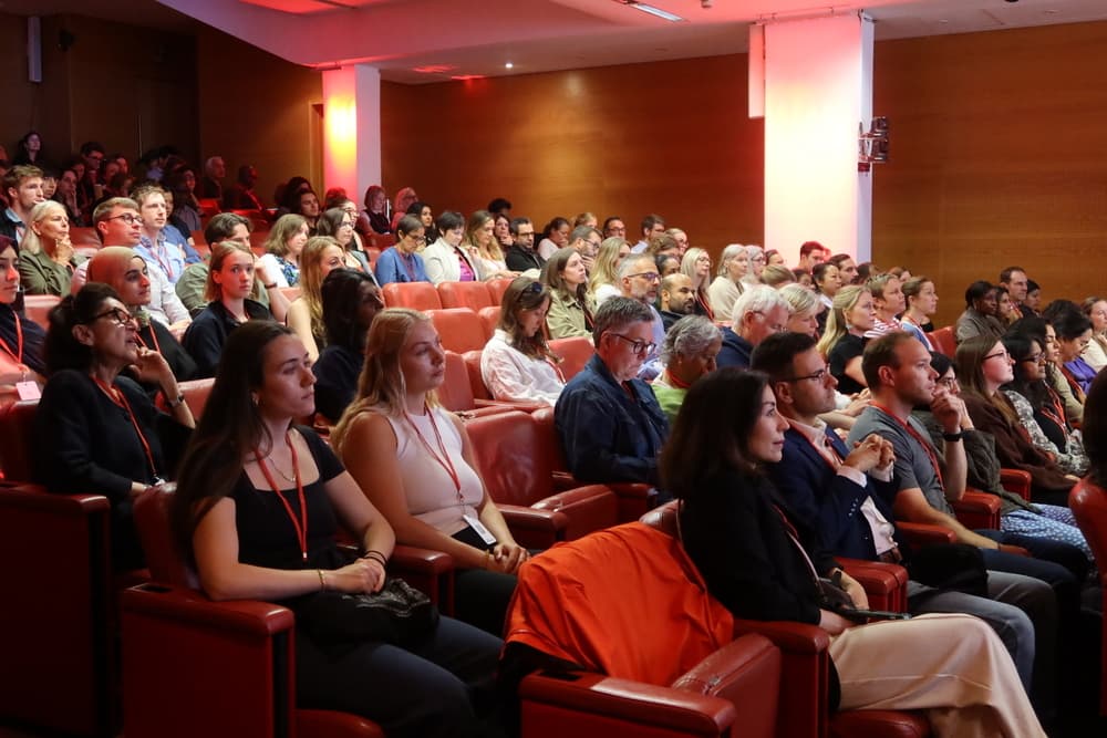 People in a dark auditorium audience look towards the front of the room